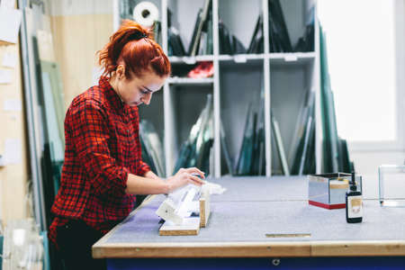 Woman glazier worker sticking together glass panes with ultraviolet lamp. Industry, manual workの写真素材