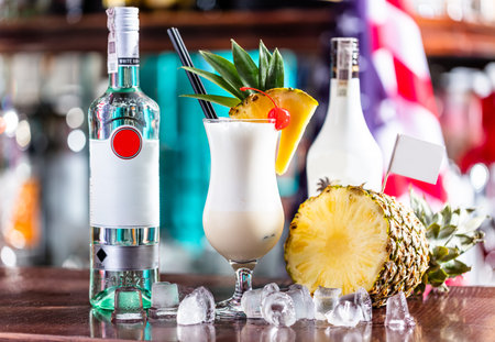 Pina colada coctail on bar counter with fresh pinapple and alcohol bottles.