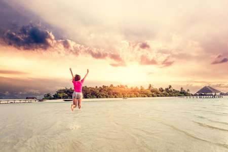 Young woman jumping for joy in Maldives at sunset. Exotic holiday destinationの写真素材