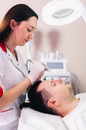 Cosmetologist doing hydrafacial treatment on man face in beauty clinicの写真素材