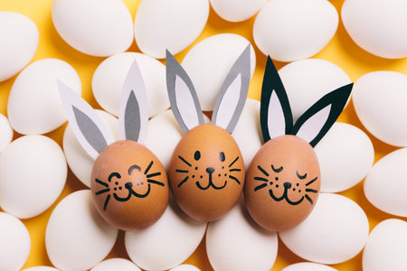 Easter egg with painted smiling bunny face and ears. Lying on white eggsの写真素材