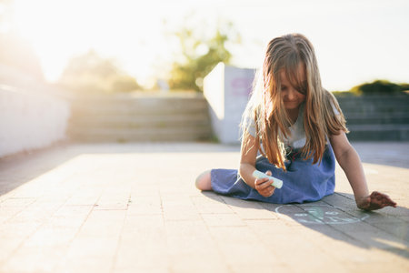 Kid drawing on pavement in urban neighborhood and smiling at summerの写真素材