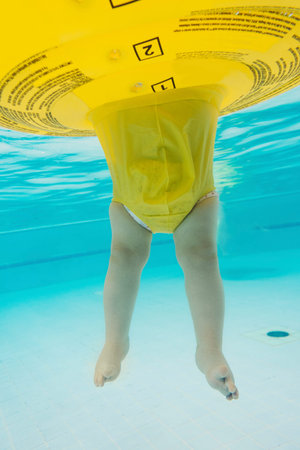 Baby toddler learning to swim in the pool in swim ring, underwater view