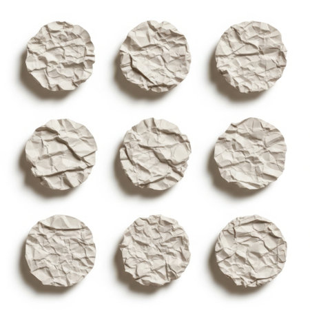 This image depicts a collection of nine crumpled paper balls arranged in a 3x3 grid against a white background. The papers are white and appear to be crumpled in various ways, creating a textured and uneven surface. The lighting highlights the folds and creases, giving the image a three-dimensional effect.の素材