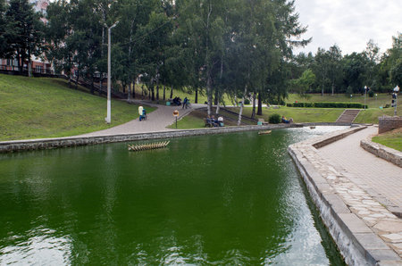 City Park, recreation area with an artificial pond and paved alleys, where the people strolling on a cloudy summer day.の写真素材