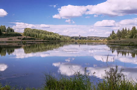 Summer view of the water surface of the river with overgrown picturesque banks and Cumulus clouds in the blue sky, toned.の写真素材