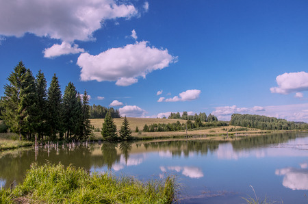 Summer view of the water surface of the river with overgrown picturesque banks and Cumulus clouds in the blue sky, toned.の写真素材