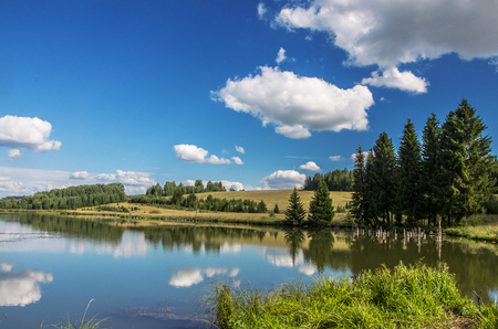 Summer view of the water surface of the river with overgrown picturesque banks and Cumulus clouds in the blue sky.の写真素材