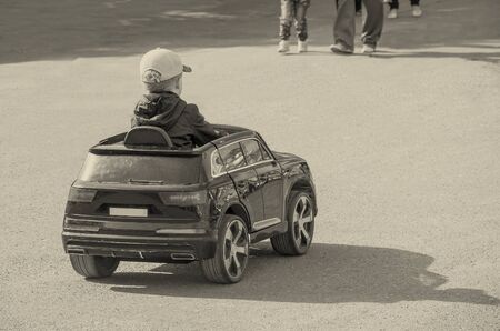 The child is engaged in driving a children's electric car on a flat ground on a warm summer day, close up, copy space.の写真素材