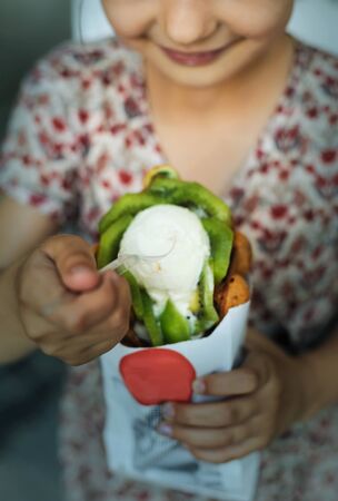 Girl is eating a ice cream with fruits and waffle bubbles outdoors.の写真素材
