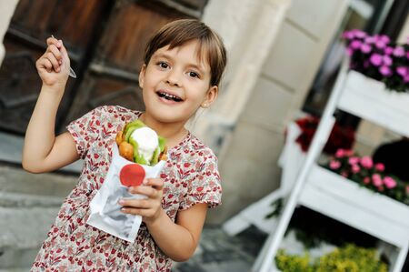 Girl is eating a ice cream with fruits and waffle bubbles outdoors.の写真素材