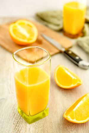 Orange juice in a glass and slices of oranges. Cutting board and knife in the background.の写真素材