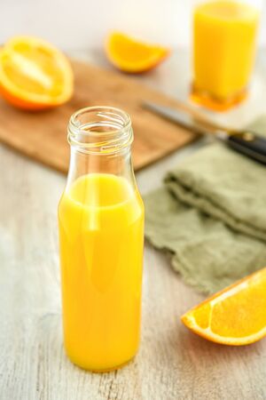 Orange juice in a bottle and slices of oranges. Cutting board and knife in the background.の写真素材