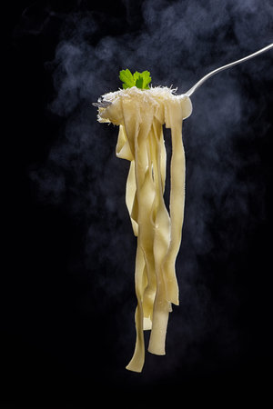 The noodle is steaming on the fork on a dark background. Low key.