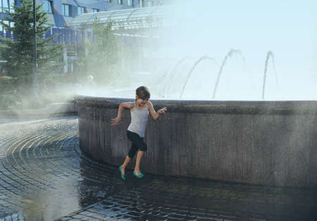The seven-year-old girl is runing in a splash of fountain water.の写真素材
