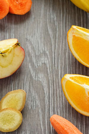There are carrots, banana, orange, apple and ginger on a wooden background.の写真素材