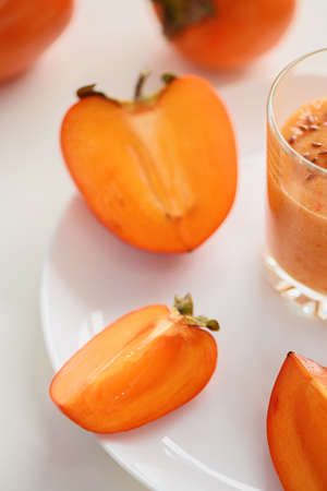 Slices of ripe persimmon on a white plate. There is a glass with a smoothie nearby.の写真素材