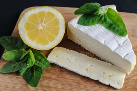 A piece of Brie cheese, lemon and spinach are on the cutting board.の写真素材
