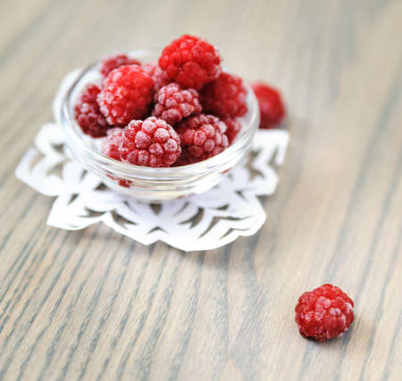 Frozen raspberries in a glass bowl on a wooden table.の写真素材