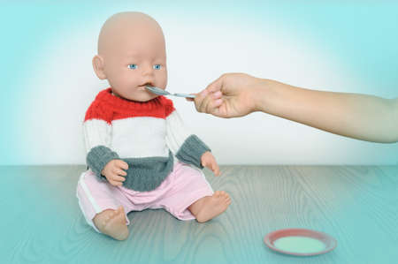Children's hand is holding the spoon and feeding the doll.の写真素材