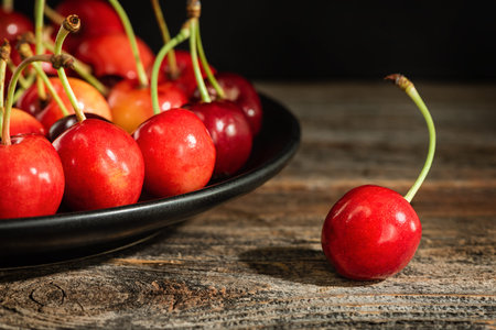 Sweet cherries on a plate on a wooden surface. Low key.