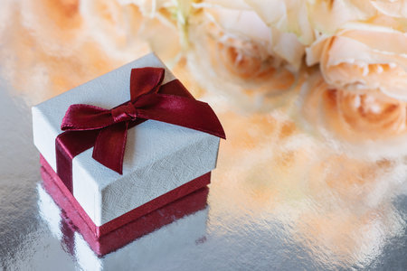 The gift box is on a silver surface on the background of yellow roses.