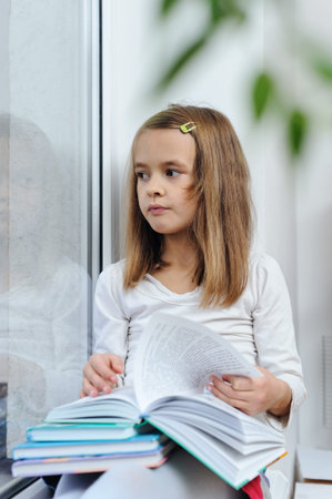 The girl is sitting on the window sill and reading a book.