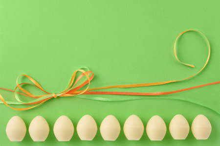 Easter still life. White chocolate eggs and colored ribbons on the green background. Copy space.