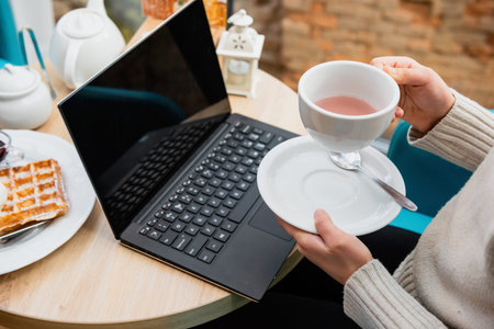 Girl is drinking tea in a cafe at a table with a laptop.