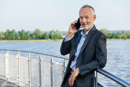 Smiling businessman in a gray suit with a smartphone.の写真素材