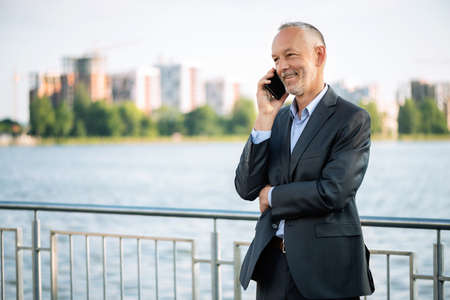 Smiling businessman in a gray suit with a smartphone.の写真素材