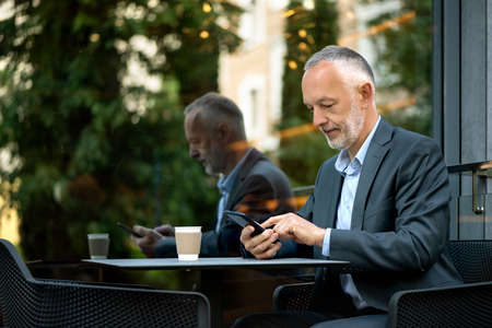 Smiling businessman in a gray suit with a smartphone.の写真素材