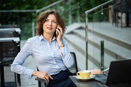 Beautiful business woman is talking on a smartphone. She is sitting at a table in a restaurant.の写真素材