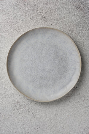 The light gray plate with dark gray splashes on a light grained background. top view.の写真素材
