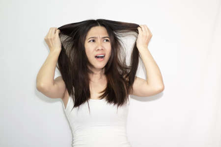 Asian beautiful women wear white t-shirt are pulling and watching messy hair with worry and unhappy cause by hair lossの写真素材