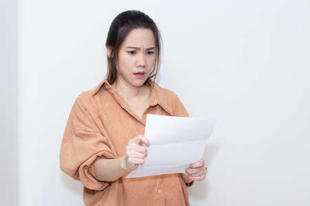 Asian woman are looking at bill or invoice that it is overdue and huge of debt with worried and shocked face. No money for paying.の写真素材