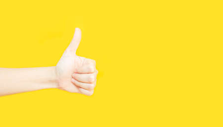 woman's hand with thumbs up gesture  in copy space area for advertisement promotion or text on yellow backgroundの写真素材