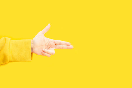 Woman's hand making gun gesture and pointing to copy space area on yellow background.
