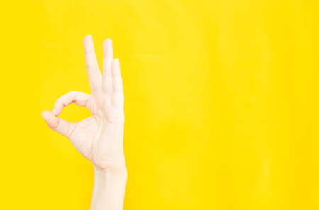 woman's hand with OK or agreement gesture  in copy space area for advertisement promotion or text on yellow backgroundの写真素材
