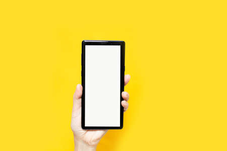 Woman's hand are holding smartphone with white screen on yellow background for advertising and promotion.の写真素材