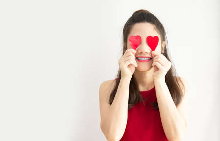 Asian beautiful woman with red theme are holding red heart shape paper covering her eyes with smiling and happinessの写真素材