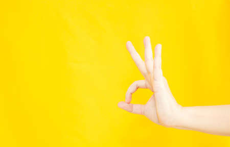 woman's hand with OK or agreement gesture  in copy space area for advertisement promotion or text on yellow backgroundの写真素材