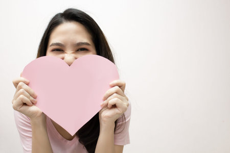 Asian beautiful woman  are holding Pink heart shape paper  covering her mouth  with smile and happiness. Valentine day and Love.の写真素材