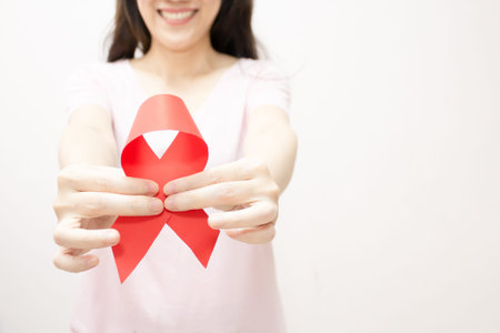 Asian woman are hold and present red ribbon in front of her face for AIDS campaign to encourage and...