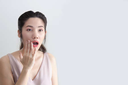 Asian beautiful woman raise hand touching her lip and open mouth and looking away with shocking and surprisingの写真素材