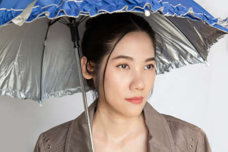 Unhappy Asian beautiful woman hold a colored umbrella with lonely and look away on rainy dayの写真素材
