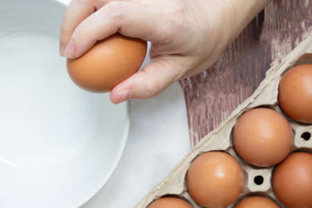 A woman's hand is cracking fresh egg at bowl to prepare for cookingの写真素材