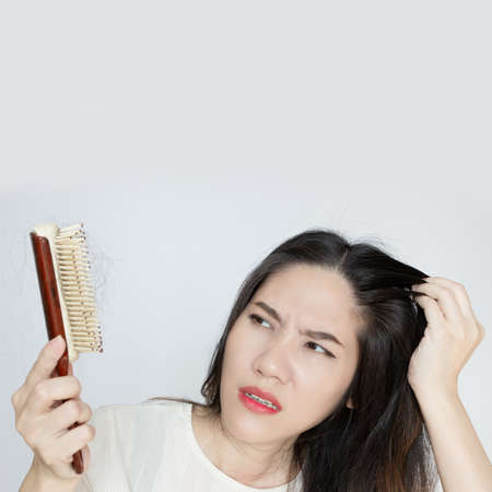 Asian beautiful woman are looking   her hair loss on brush and touch head with shocked and a worry face.の写真素材