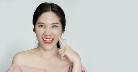 Asian beautiful woman use indicated finger touch on cheek and smile mouth open with proud of skinの写真素材