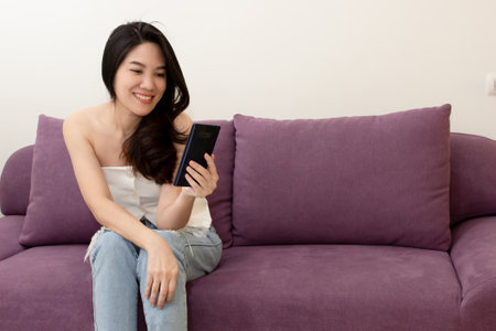 Asian beautiful woman sitting on sofa  use smart phone to chat or shopping online or on social media on her holiday with a happiness and smileの写真素材